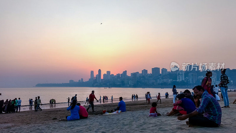 2019年5月20日，印度，马哈拉施特拉邦，孟买:人们坐在Girgaum Chowpatty广场上，身后是孟买的天际线和夕阳。
